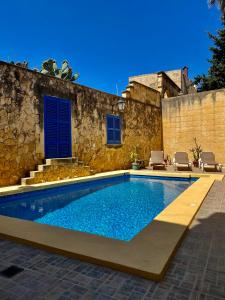 a swimming pool in front of a stone building with blue doors at MJ Farmhouse B&B in Xagħra