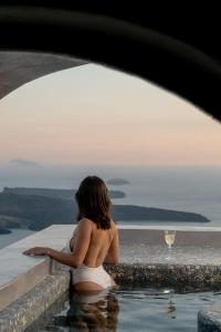 a woman sitting in a swimming pool with a glass of wine at Ventus Paradiso Villa in Imerovigli