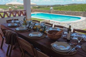 a wooden table with plates and wine glasses and a swimming pool at Horta dos Caracóis in Borba