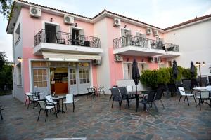 eine Terrasse mit Tischen und Stühlen vor einem rosa Gebäude in der Unterkunft Anaxos Bay Rooms & Apartments in Anaxos