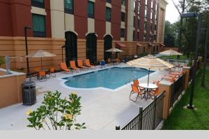 una piscina con sillas, mesas y sombrillas junto a un edificio en Hampton Inn & Suites Albany at Albany Mall, en Albany