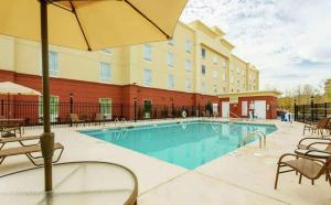 奥古斯塔Hampton Inn Augusta Fort Eisenhower的酒店的游泳池，配有椅子和遮阳伞