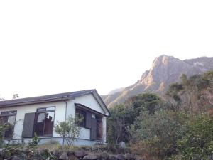 uma casa branca com uma montanha ao fundo em Minshuku nicoichi em Yakushima