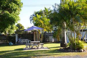 una mesa de picnic y una sombrilla en un patio con palmeras en Rover Motel, en Mackay