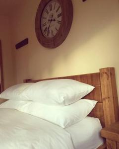 a clock on the wall above a bed with pillows at Bumbleberry Cottage in Gresford