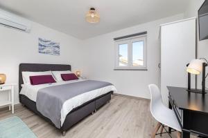 a white bedroom with a large bed and a desk at Apartman Milazzi in Baška