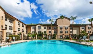 een zwembad tegenover een hotel met palmbomen bij Homewood Suites by Hilton Brownsville in Brownsville