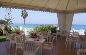 a restaurant with white tables and chairs and the ocean at Cala Petrosa Resort in Parghelia
