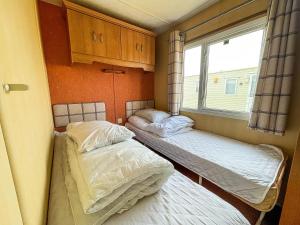 two beds in a small room with a window at Spacious Caravan For Hire With Decking By The Beach In Suffolk Ref 40094nd in Lowestoft