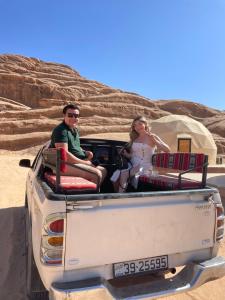 mężczyzna i kobieta siedzący z tyłu ciężarówki w obiekcie Zarb Desert Camp w mieście Wadi Rum