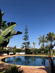 ein großer Pool mit Palmen im Hintergrund in der Unterkunft BOUZNIKA BAY COUNTRY CLUB in Bouznika