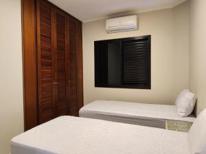a bedroom with two beds and a window and a tv at Flats Capitania Varam Pitangueiras in Guarujá