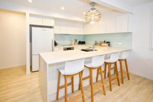 a kitchen with white cabinets and a counter with bar stools at Stylish 2 b/r apartment - 4 guests, garage ZC5 in Alexandra Headland