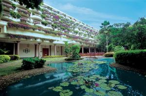 un bâtiment avec un étang avec des nénuphars devant lui dans l'établissement The Oberoi Bengaluru, à Bangalore