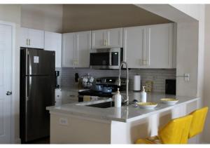 a kitchen with white cabinets and a stainless steel refrigerator at The Aliyah Poolside View with Luxe Pool, Gym, & Theater in Houston