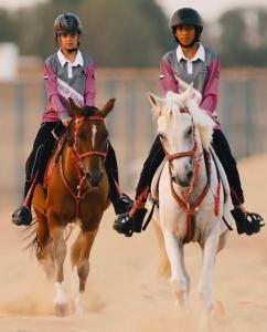 two people riding horses on a dirt field at اسطبلات أساور للفروسية Asawer Equestrian Stables 