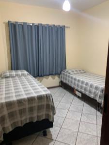 two beds in a room with blue curtains at Solar de Bruna - Apartamento com 2 Qts - 1 Suíte - Garagem coberta - Wi-Fi - Netflix - Acomoda 6 pessoas a 70 metros da praia in Guarapari
