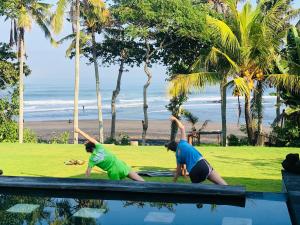two women are doing yoga near a pool with the beach at Bali Natha Beach Front in Canggu