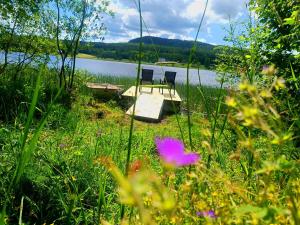 two chairs and a table in the grass near a lake at Lila Stuga in Väja