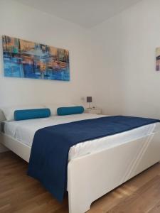 a white bed with a blue blanket and a painting on the wall at Aura Apartments - Orizzonte Turismo in Porto Cesareo