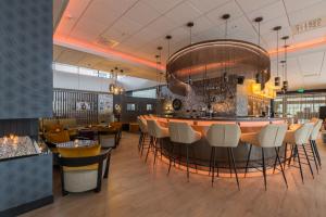 a restaurant with a bar with white chairs at Leonardo Royal Hotel Den Haag Promenade in The Hague