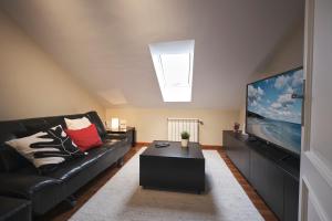 ein Wohnzimmer mit einem schwarzen Sofa und einem Flachbild-TV in der Unterkunft camiño dos faros in Ponteceso