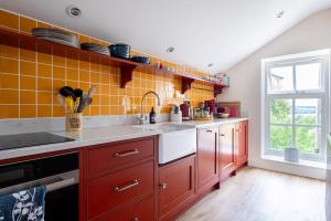 a kitchen with red cabinets and yellow tiles at Deerpark Barn in Daventry