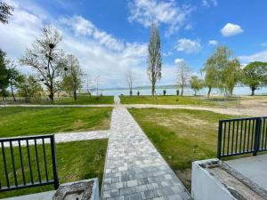 a walkway through a park with trees and the water at Gyöngybagoly Apartman in Balatonberény