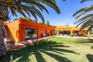 an orange house with a lawn and palm trees at Unique Villa -1 km to Beach, private Natural pool, Tennis Court & Jumping Mat in Sagres