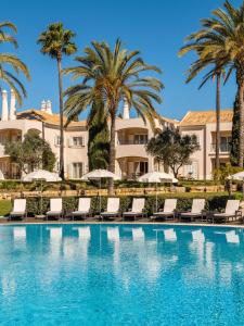 a pool with chairs and palm trees in front of a building at Vale d'Oliveiras Quinta Resort & Spa in Carvoeiro