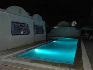 uma piscina à noite com iluminação azul em Belle maison en face de la mer em El Maamoura