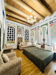 a room with a bed and a couch and paintings on the walls at Komil Bukhara Boutique Hotel in Bukhara