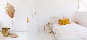 a white bedroom with a bed with a yellow pillow at Boho Beach Retreat in La Lucia, Umhlanga in Durban