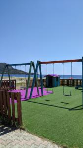 um parque infantil com baloiços roxos e a praia em Backyard houses em Torone