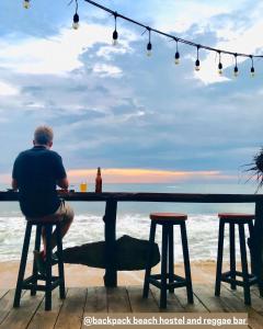un hombre sentado en una mesa mirando el océano en Backpack Beach Hostel & Reggae Bar en Galle