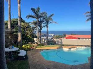 a swimming pool with a table and palm trees and the ocean at Lazydaze Point in Jeffreys Bay