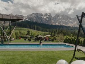 una mujer parada en una piscina con montañas en el fondo en Hotel Alpenrose en Carezza al Lago