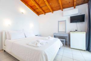 a bedroom with a bed with white sheets and a tv at Kontogoni Rooms in Elafonisos