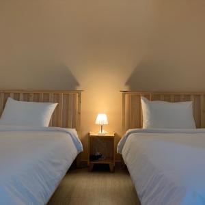 2 Betten in einem Zimmer mit einer Lampe auf einem Nachttisch in der Unterkunft Hostel Espace in Chuncheon