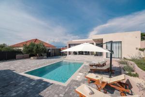 a swimming pool with chairs and an umbrella and a house at VILLA ARGOLA in Vrsi