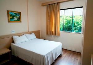 Un dormitorio con una cama blanca y una ventana grande. en Hotel Dan Inn Poços de Caldas - A melhor localização do Centro by Nacional Inn, en Poços de Caldas