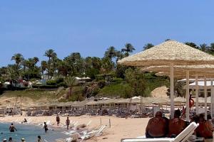 a beach with people sitting on chairs and umbrellas at ℂoral Bay Dream - Luxury Sunset Sea View Apartment in Sharm El Sheikh