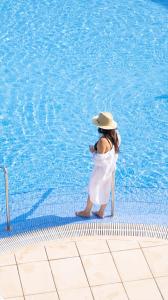 una donna con un cappello in piedi accanto alla piscina di Seth Playa Azul a Cala'n Porter