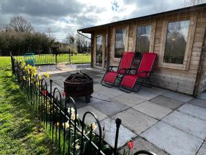 Dingestow的住宿－Silver Springs Farm Lodge，两把红色椅子放在房子旁边的庭院