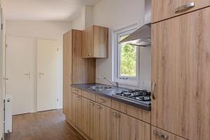 cocina con armarios de madera, fregadero y ventana en lodge De Winterkoning en Nunspeet