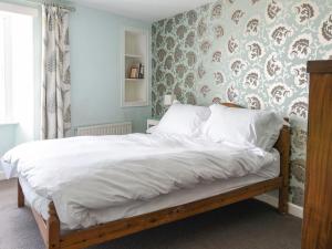 a bedroom with a bed with white sheets and floral wallpaper at Thatched Cottage in Bridport