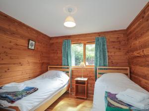 two beds in a room with wooden walls and a window at Dailfearn Chalet in Stromeferry