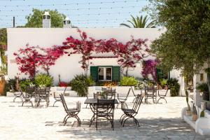 un patio con mesas, sillas y flores rosas en Masseria San Nicola Savelletri - B&B en Fasano