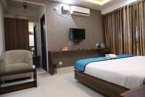 a bedroom with a bed and a chair and a tv at Western Keys Hotel in Bangalore