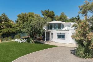 une maison blanche avec une cour avec de l'herbe et des arbres dans l'établissement Villa Tholos -Athens Riviera, à Kalívia Thorikoú
